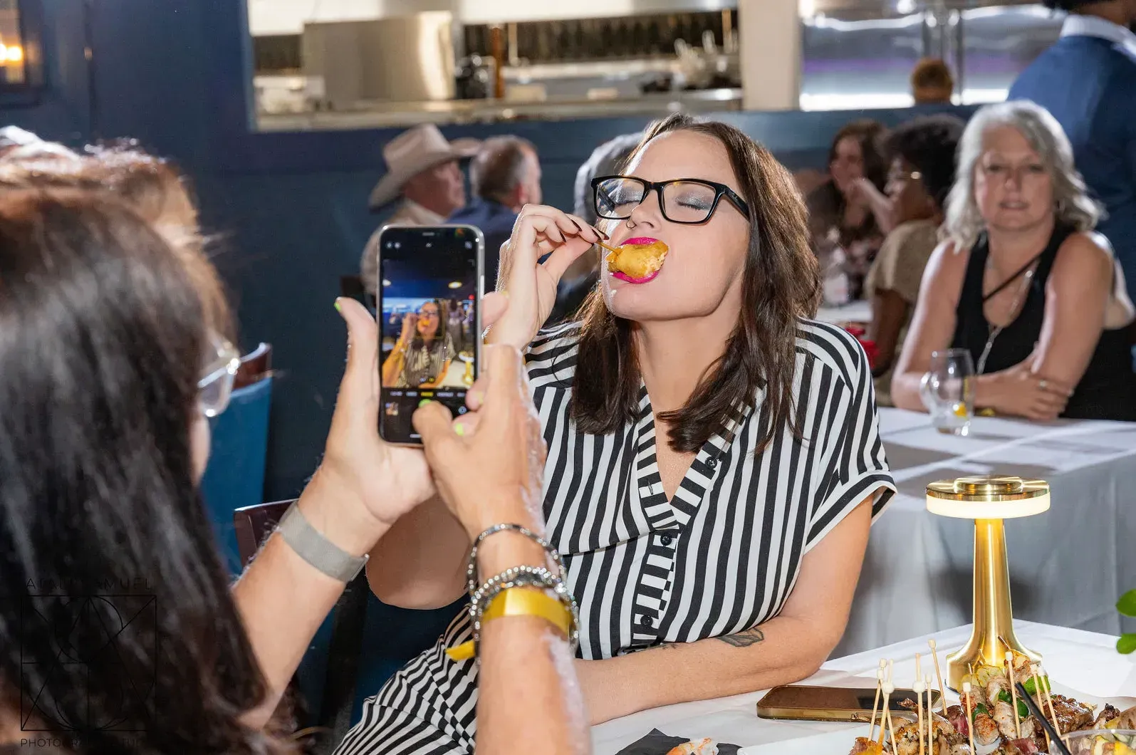 Woman in striped shirt eating food, being photographed at a restaurant.