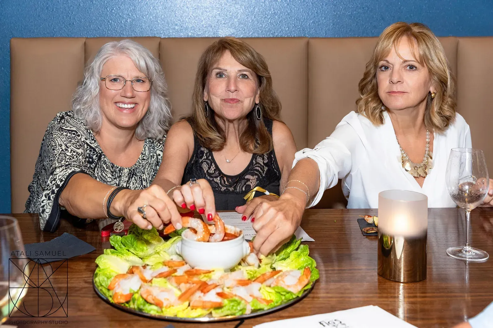 Three women at a table reaching for shrimp cocktail. They are in a restaurant.