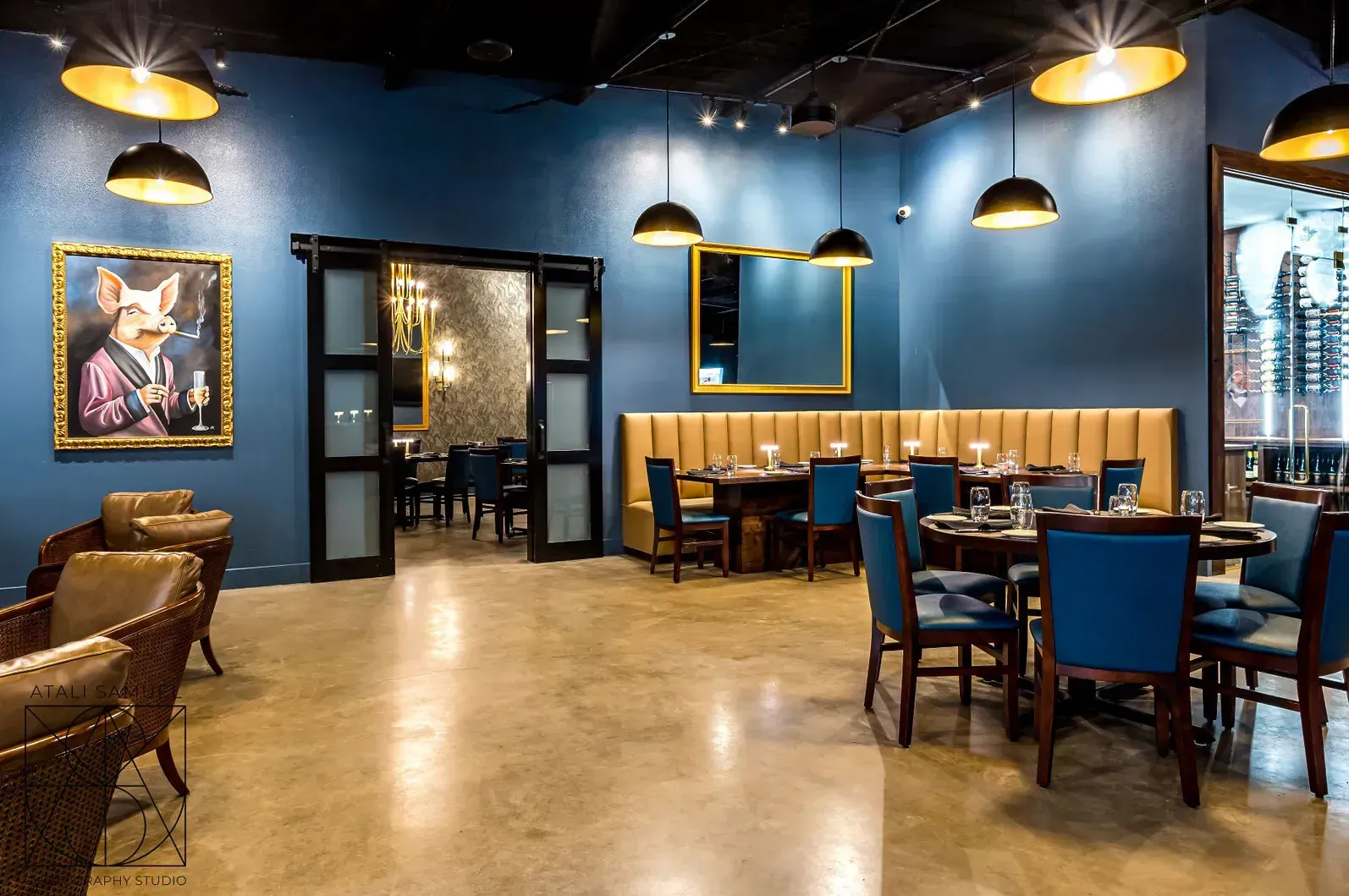 Restaurant interior with blue walls, pendant lights, tables, chairs, and artwork.