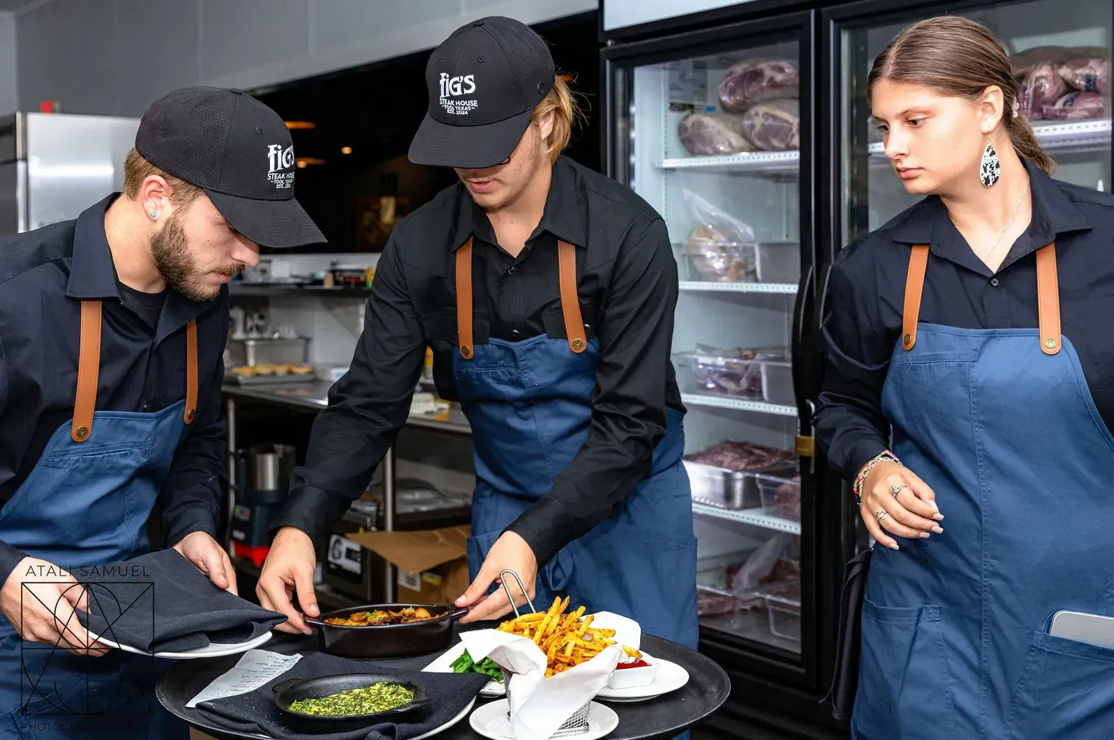 Three restaurant staff preparing food at a counter, near a refrigerated display.