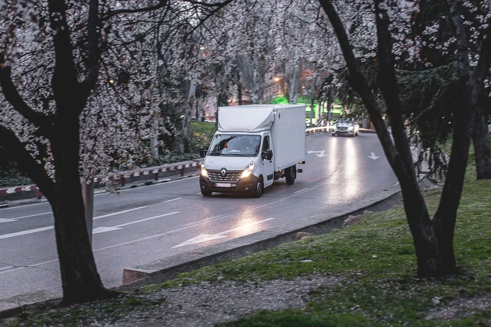 a white box truck driving on a road with cherry blossom trees around