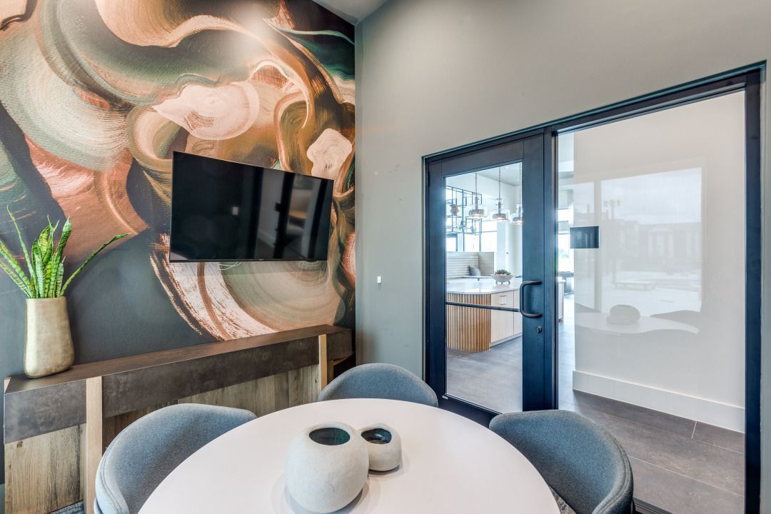 A conference room with a round table and chairs and a flat screen tv on the wall.