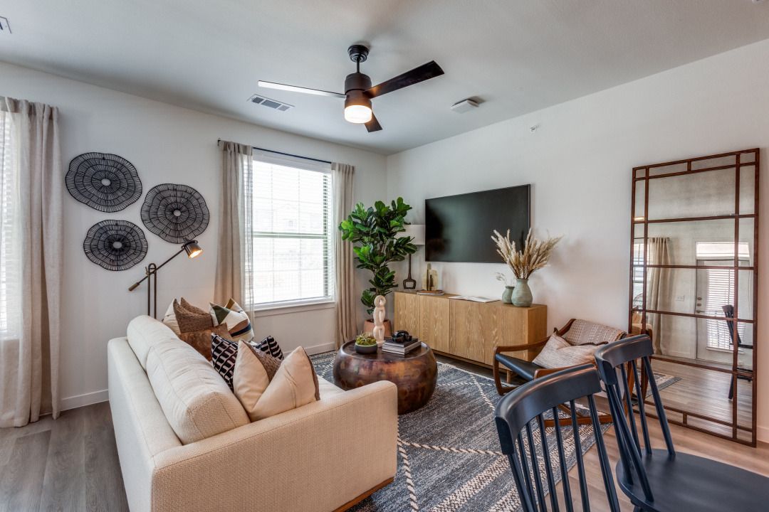 A living room with a couch , chairs , a television and a ceiling fan.