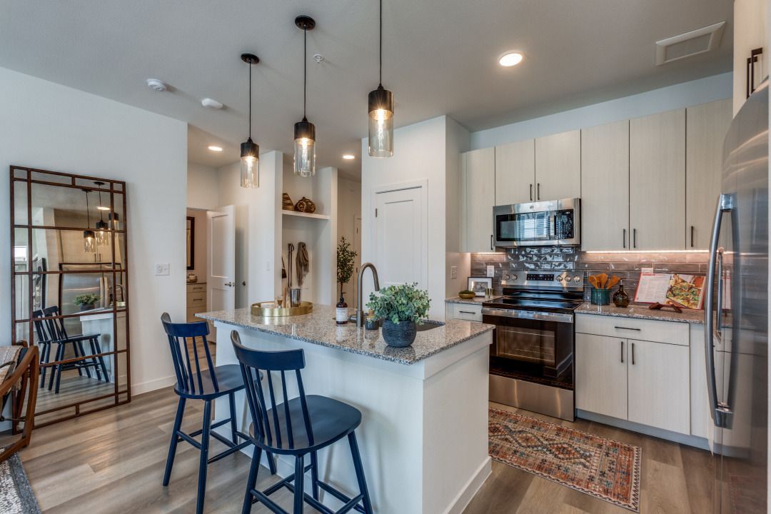 A kitchen with white cabinets , stainless steel appliances , a large island , and a mirror.