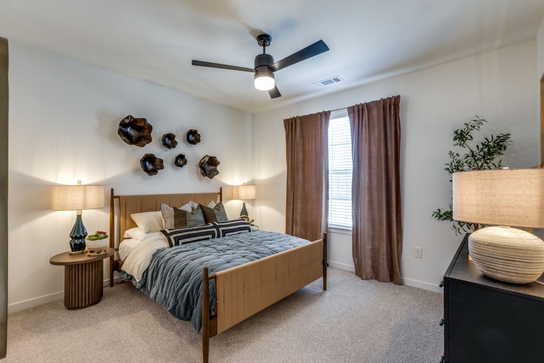 A bedroom with a bed , dresser , lamps and a ceiling fan.