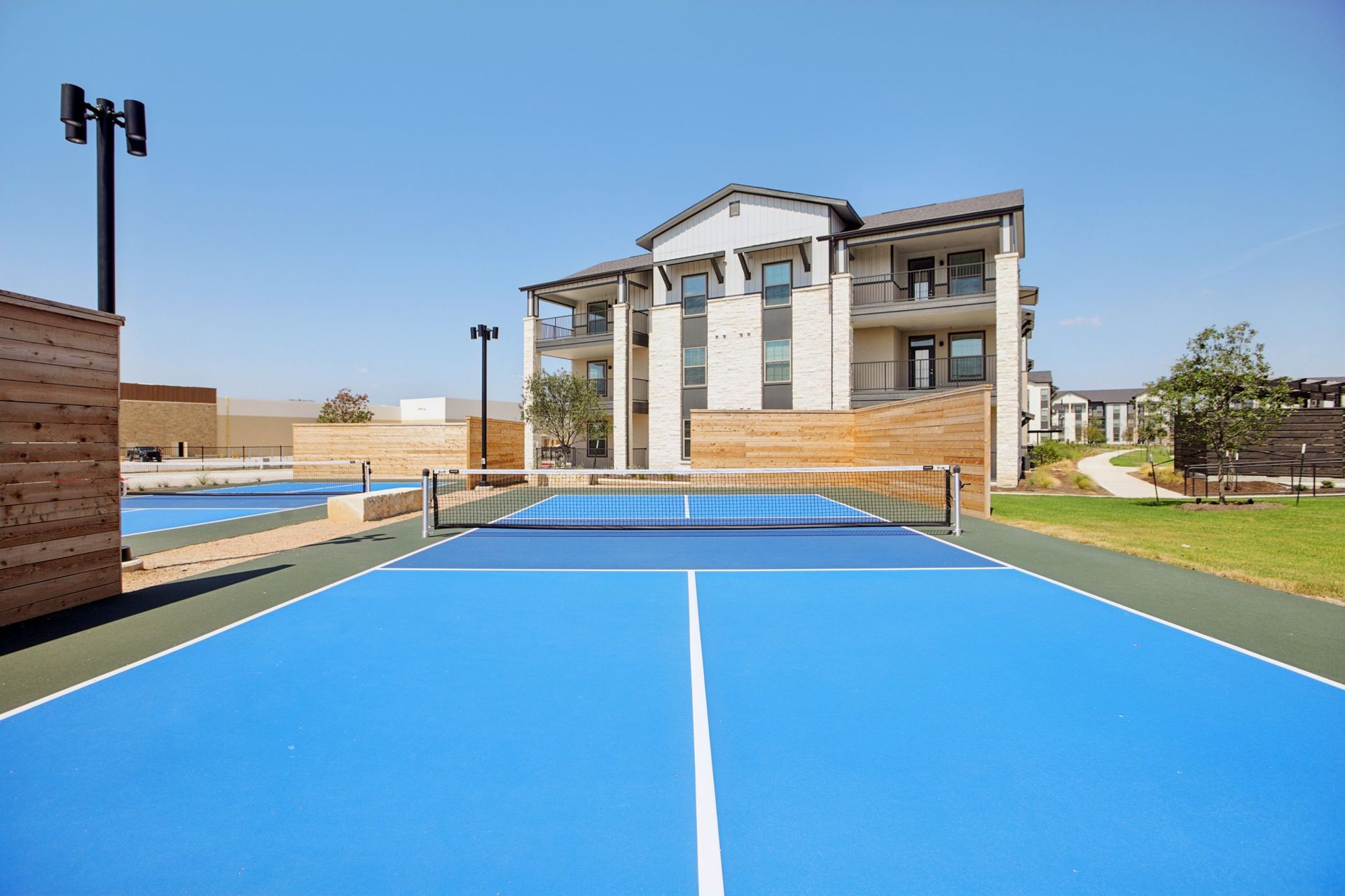 Blue pickleball court with net, building in background. Clear, sunny day.