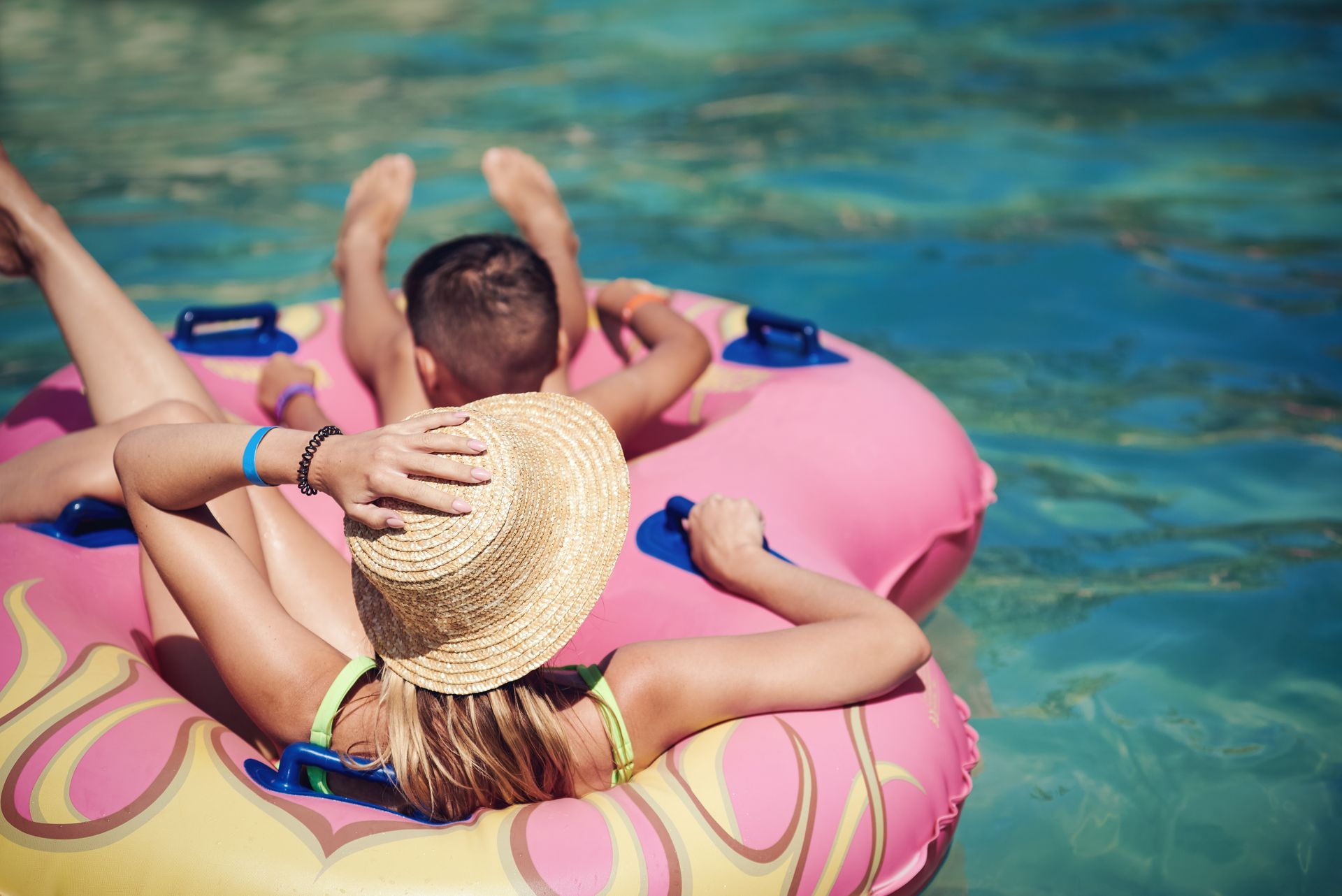 A woman and a child are floating on a pink raft in a swimming pool.