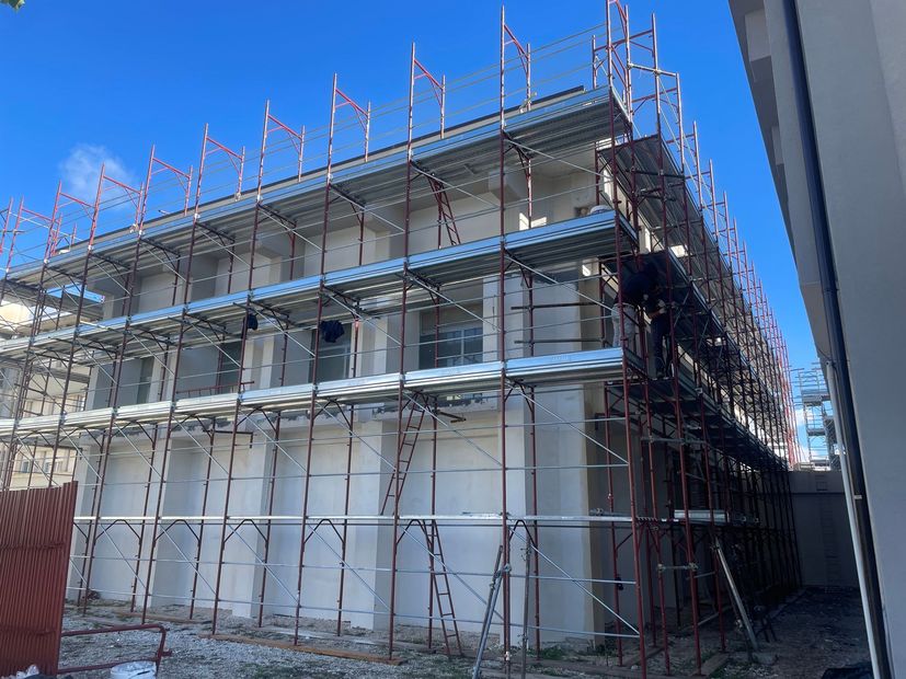 Vista aerea di un cantiere con gru e fondamenta di un edificio vicino a un'autostrada e ad alberi.