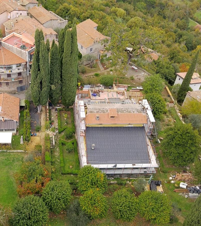 Edificio giallo con persiane marroni chiuse, auto parcheggiate sulla strada. Alberi lungo il marciapiede.