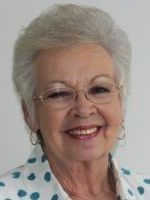 An elderly woman wearing glasses and a polka dot shirt is smiling for the camera.