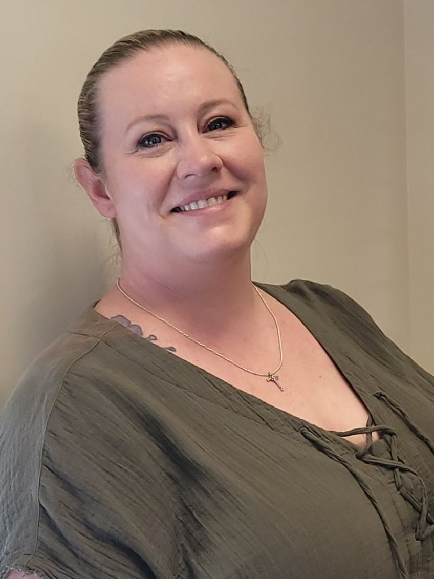 A woman wearing a green shirt and a necklace is smiling for the camera.