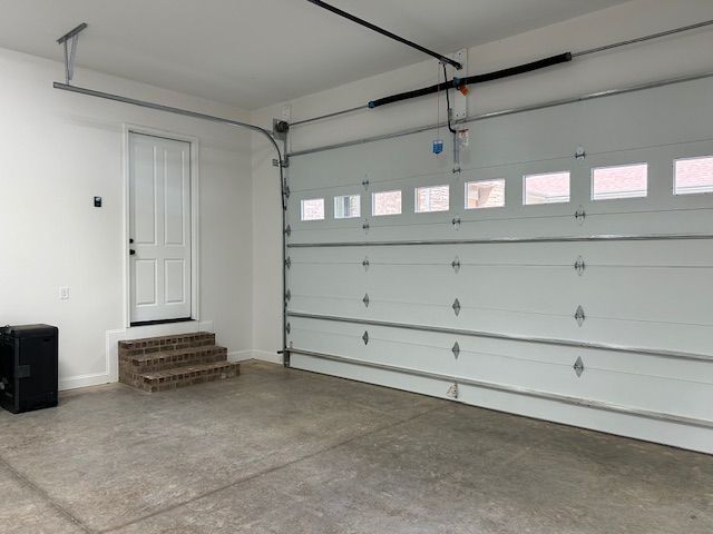 An empty garage with a white garage door and stairs leading to it.