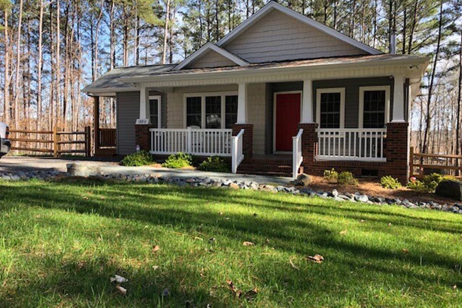 A house with a red door and a white porch is sitting on top of a lush green lawn.