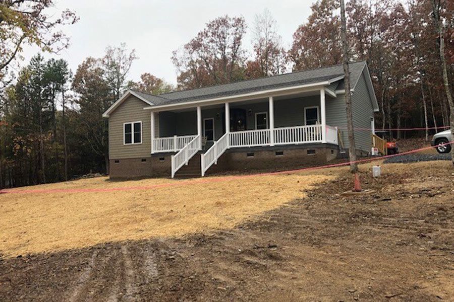 A house with a porch is sitting on top of a dirt hill.