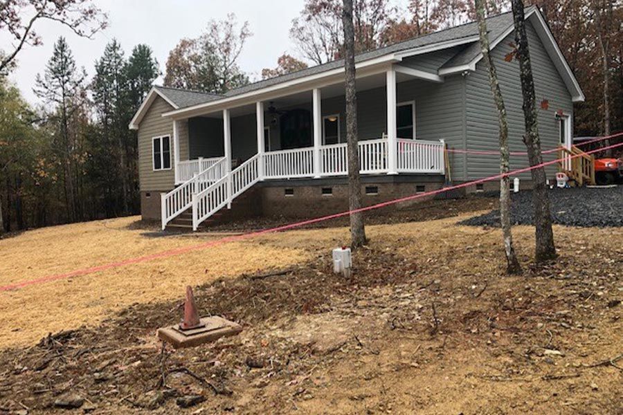 A house with a porch and stairs is sitting on top of a dirt hill.