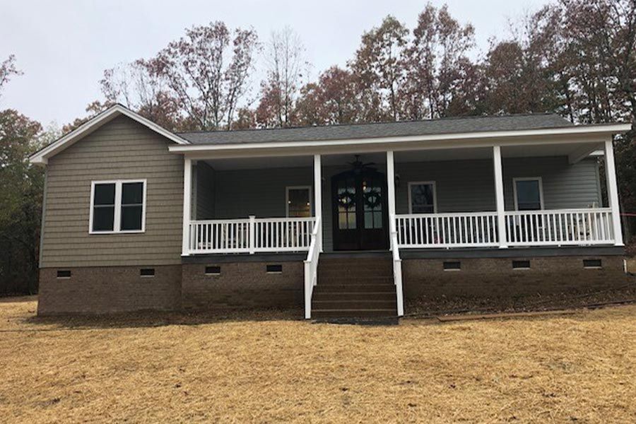 A house with a porch and stairs is sitting in the middle of a field.