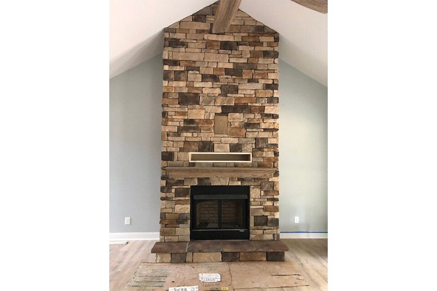 A large stone fireplace in a living room with a ceiling fan.
