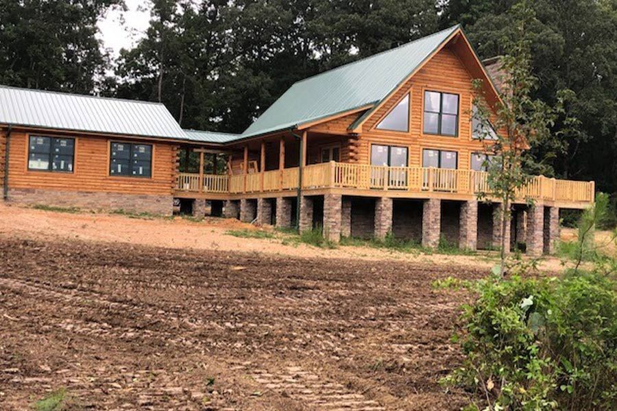 A large log cabin is sitting on top of a dirt hill.