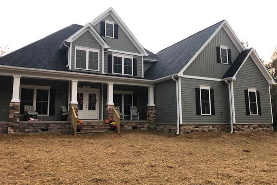 A large house with a large porch is sitting on top of a dry grass field.