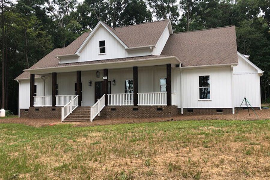A white house with a brown roof and a large porch