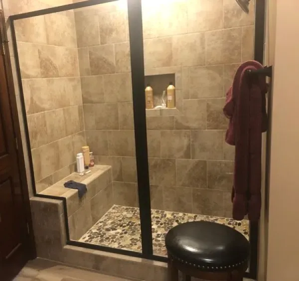 A bathroom with a walk in shower and a stool