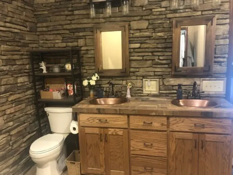 A bathroom with two sinks , a toilet , and a stone wall.