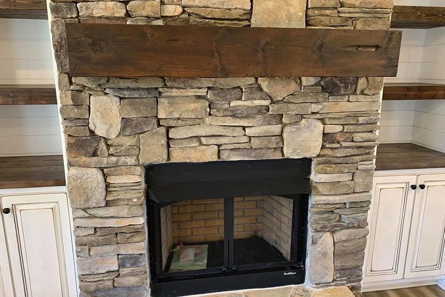 A stone fireplace with a wooden mantle in a living room.
