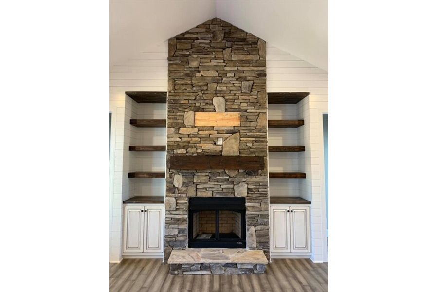 A living room with a stone fireplace and shelves.