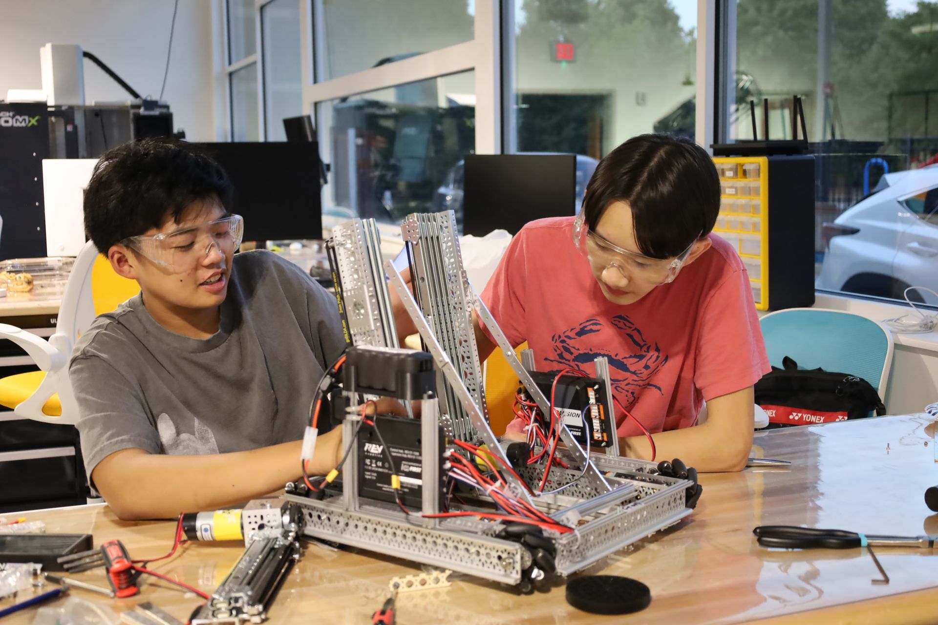 Two young men are working on a robot at a table.