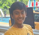 A young boy in a yellow shirt is smiling in front of a computer monitor.