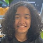 A young girl with long curly hair is smiling for the camera.