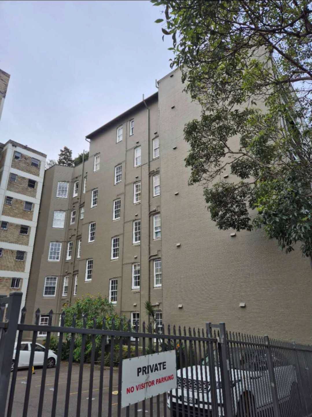 A painter in blue overalls using a roller to paint a wall light blue, standing on a ladder.