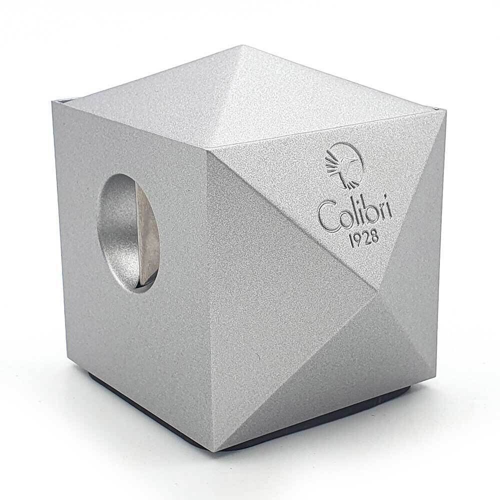Un cubo d'argento con un foro al centro è appoggiato su una superficie bianca.