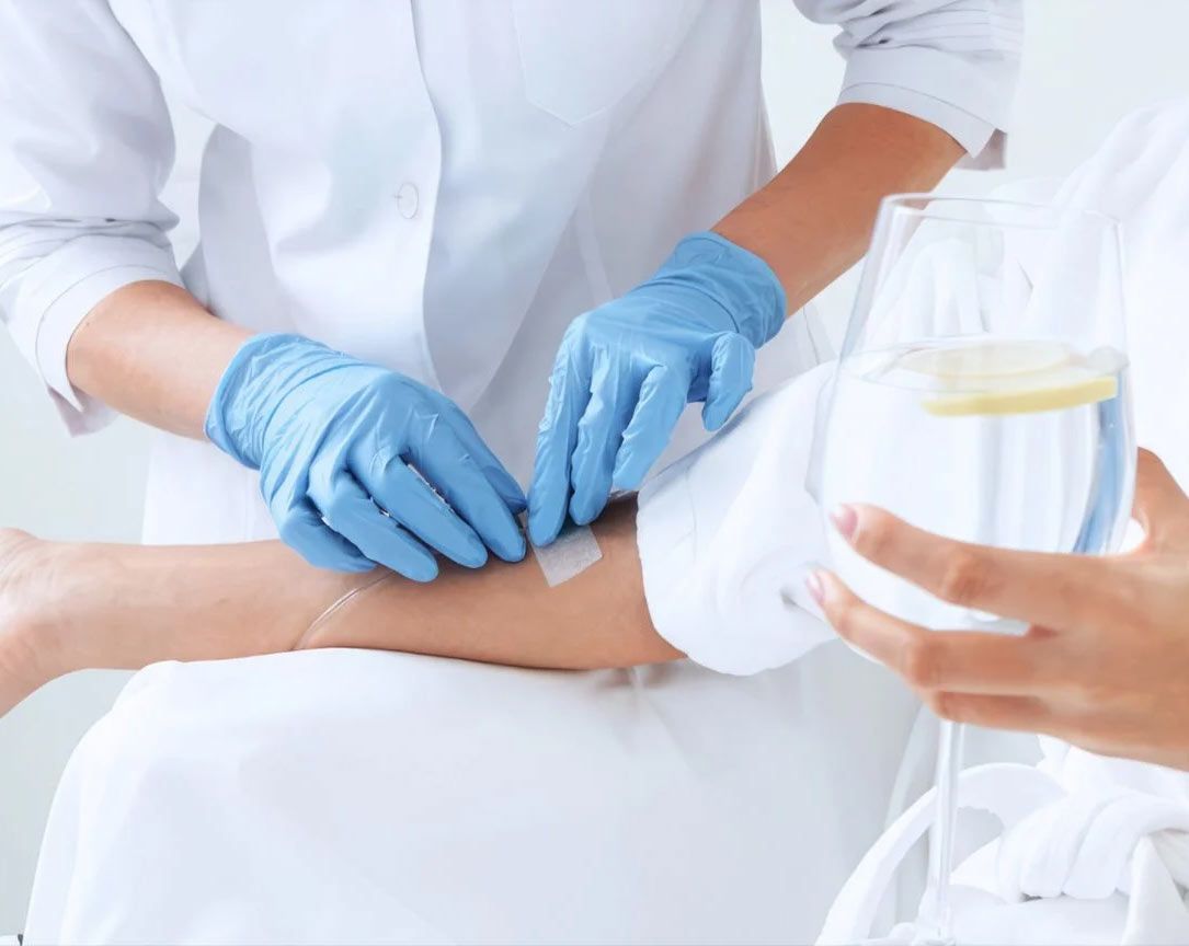 A woman is getting an injection in her arm while holding a glass of water. - IV nutrition