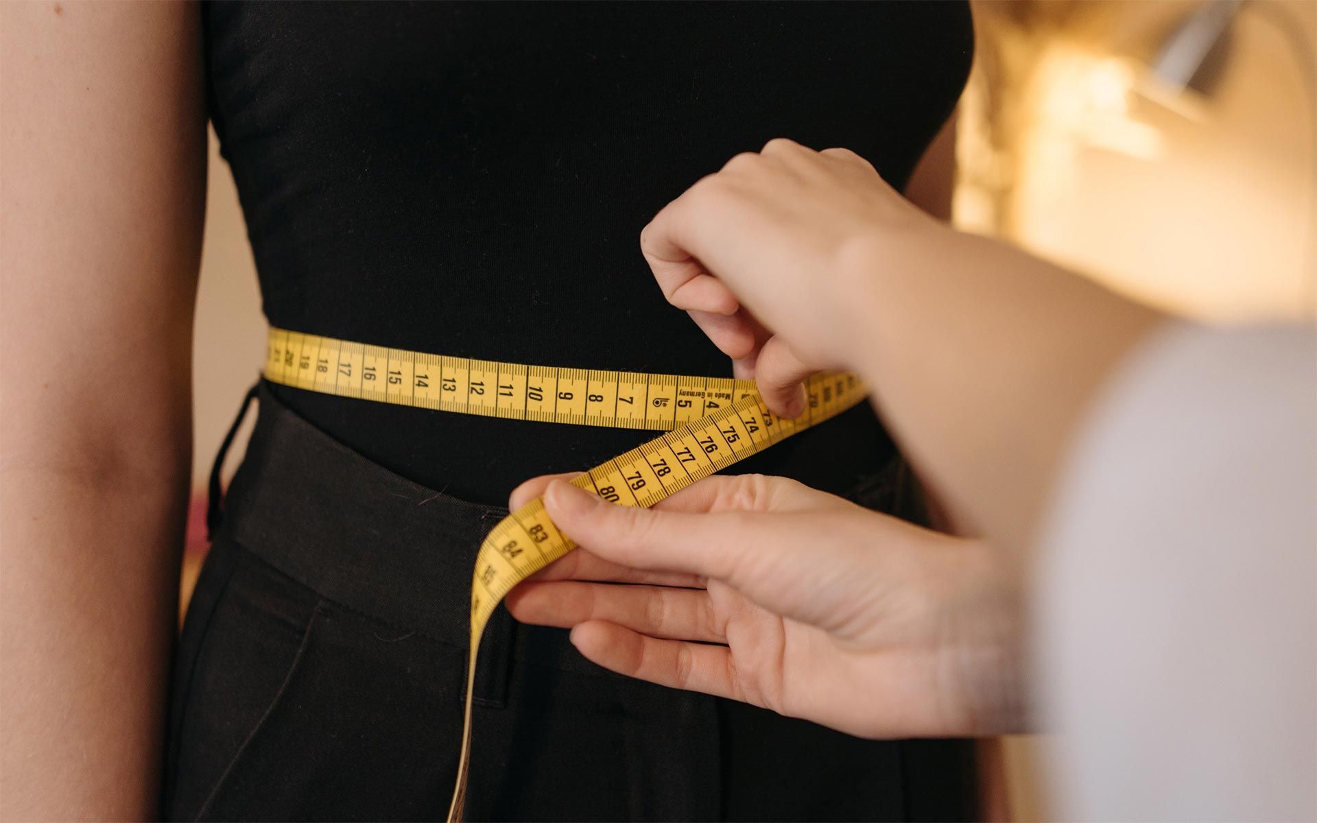 A person is measuring a woman 's waist with a tape measure. - weight loss