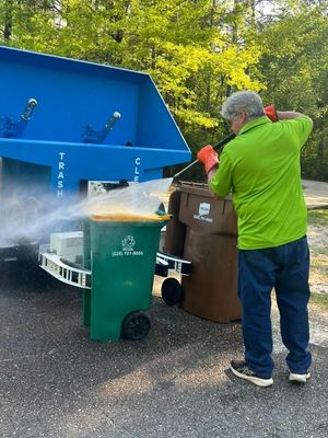 Worker in green shirt pours trash into a blue recycling truck beside bins on a street