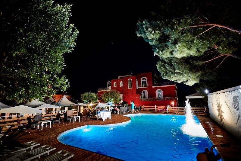 Una grande piscina è illuminata di notte di fronte a un grande edificio rosso.