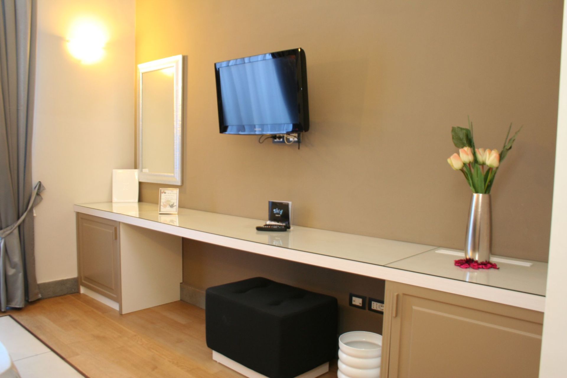 Una camera d'albergo con una scrivania e una TV a schermo piatto sulla parete.