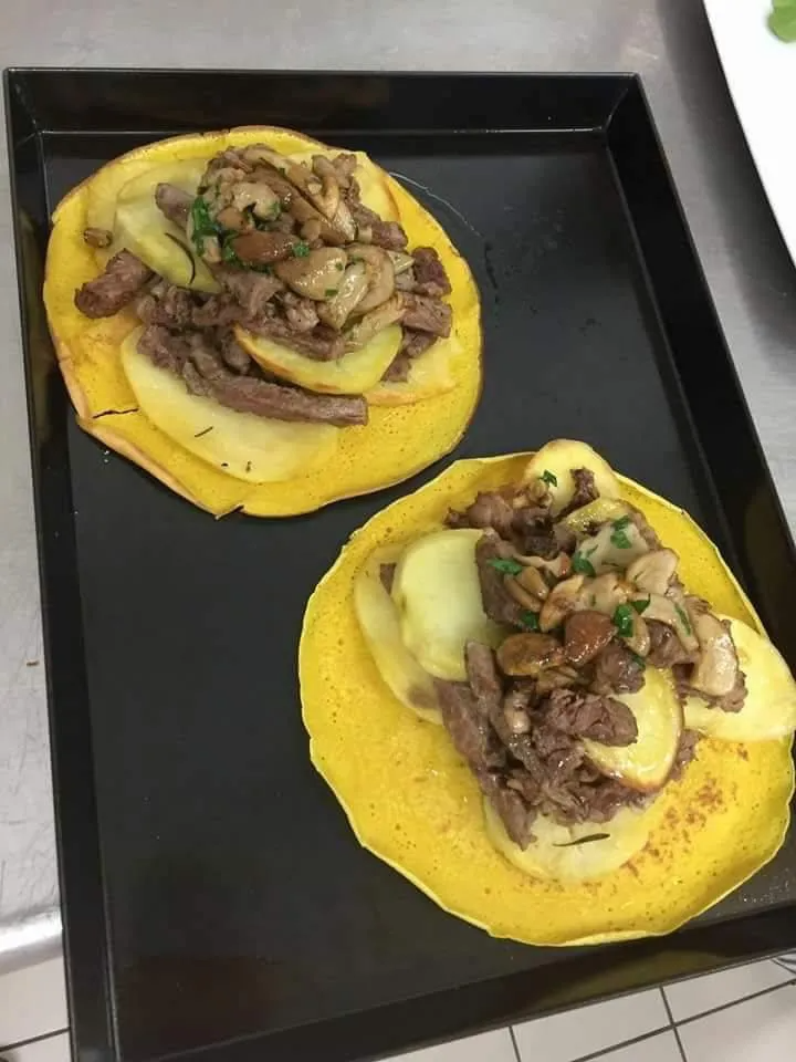 Due tacos con carne e patate su un vassoio nero.
