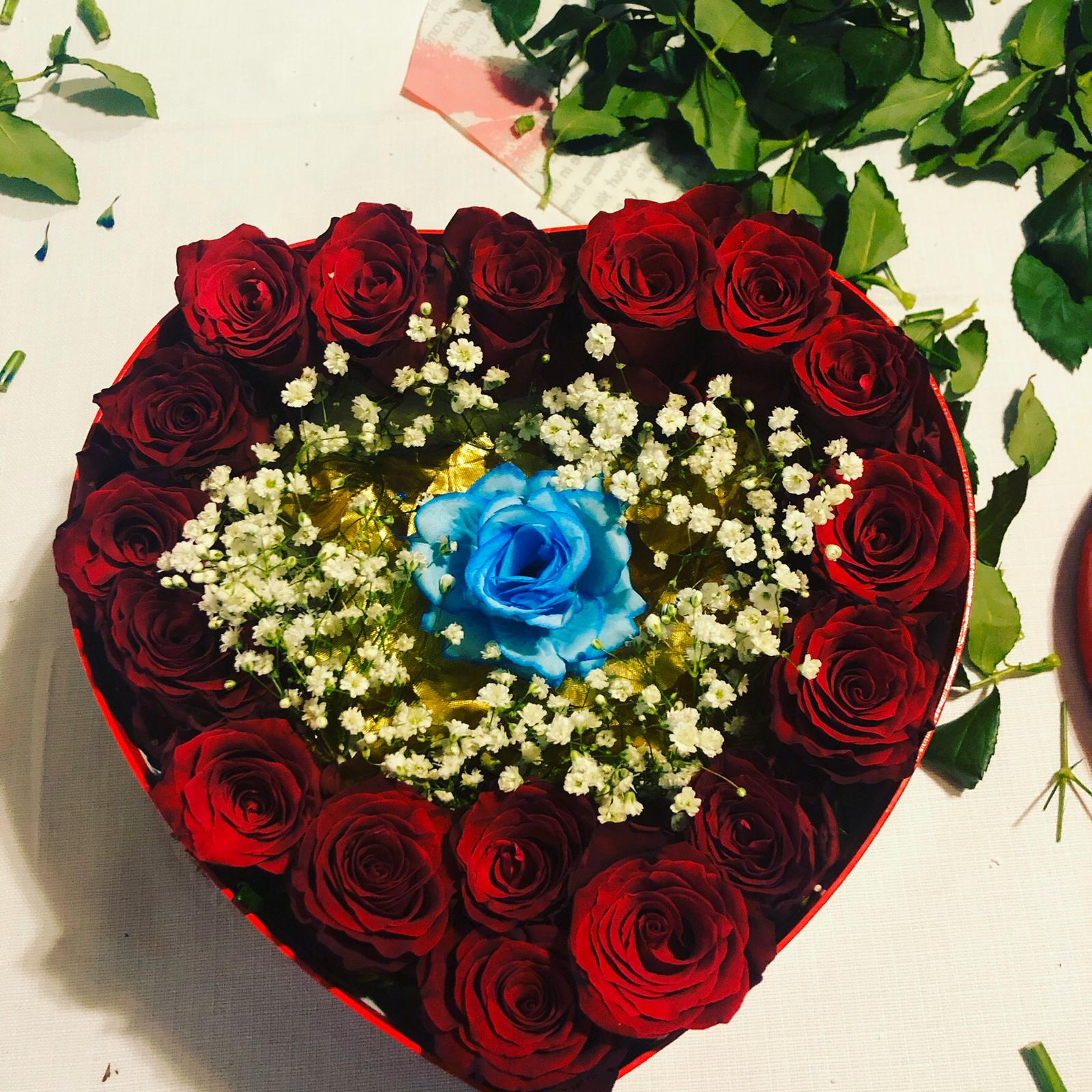 Una scatola a forma di cuore piena di rose rosse e una rosa blu
