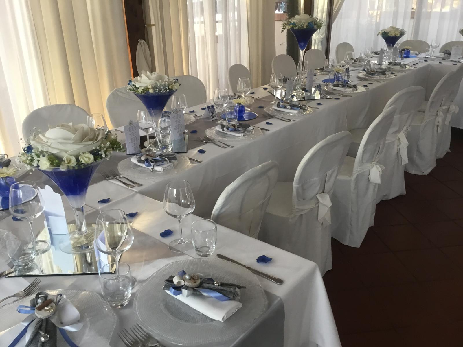 Un lungo tavolo è apparecchiato per un ricevimento di nozze con decorazioni blu e bianche.