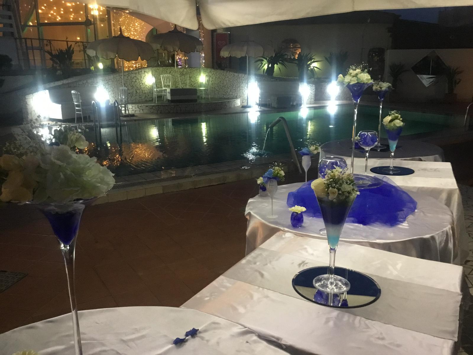 Un tavolo con un bicchiere da martini e dei fiori sopra, di fronte a una piscina.