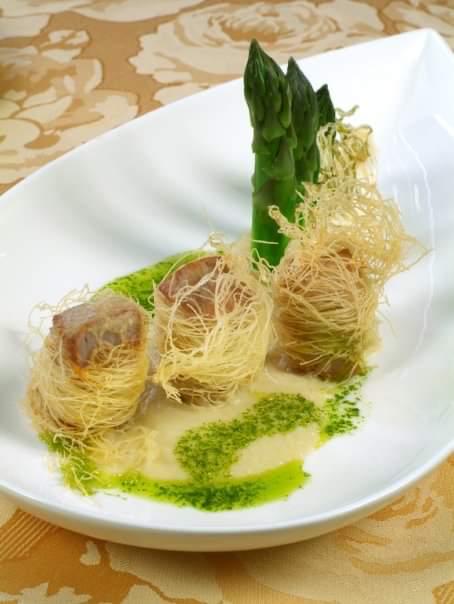 Un piatto bianco con sopra tagliatelle e asparagi su un tavolo.