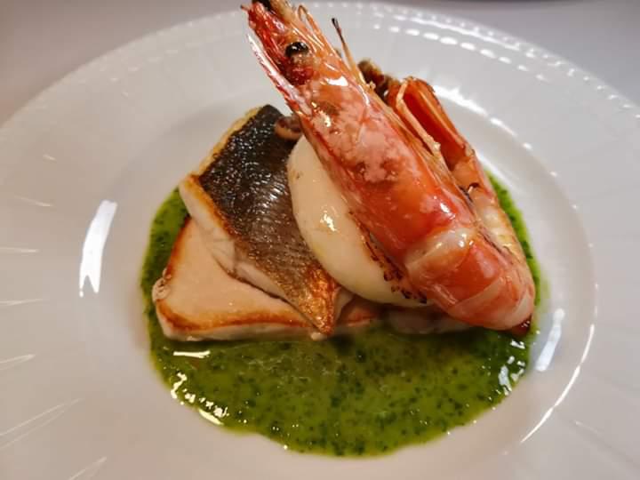 Un piatto bianco con gamberi e pesce su salsa verde