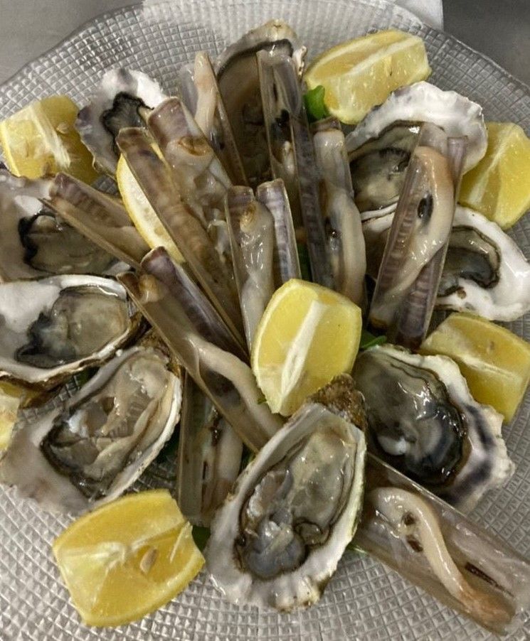 Un piatto di ostriche, vongole e fette di limone su un tavolo.