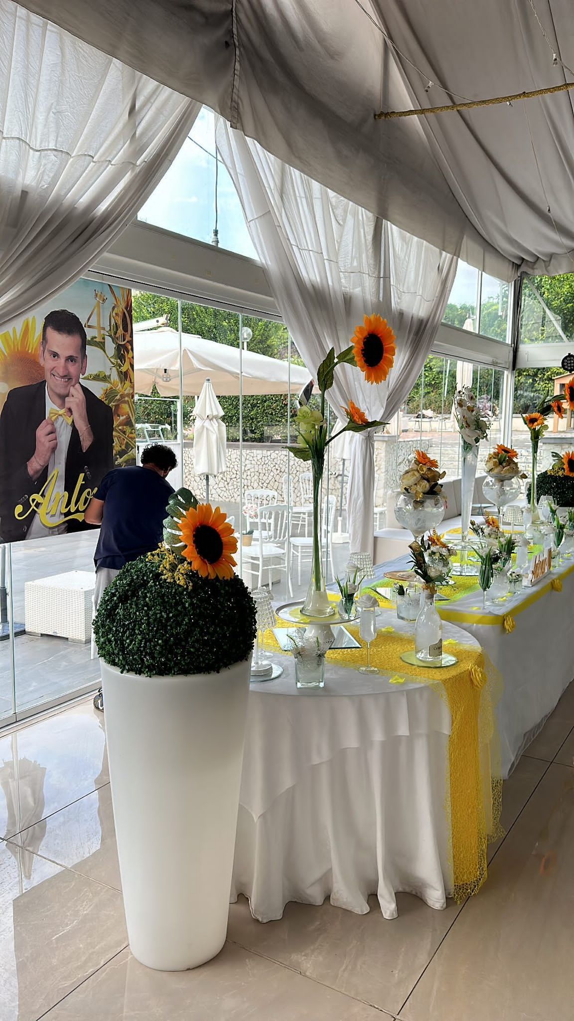 Un lungo tavolo con dei fiori e sopra il ritratto di un uomo.