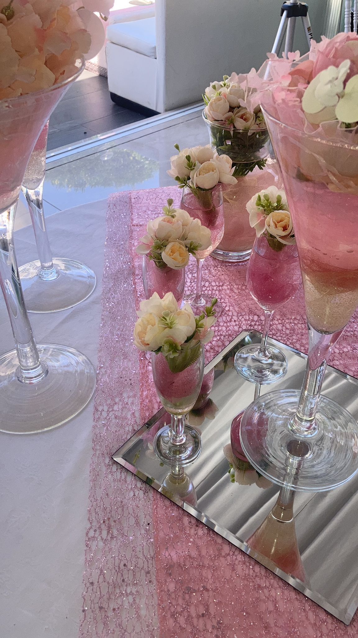 Un tavolo con fiori rosa in bicchieri da vino e uno specchio.