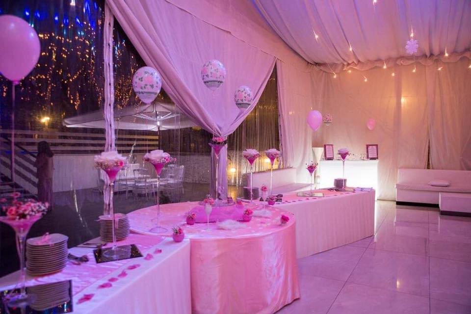 Una sala decorata in rosa e bianco per una festa con tavoli e palloncini.