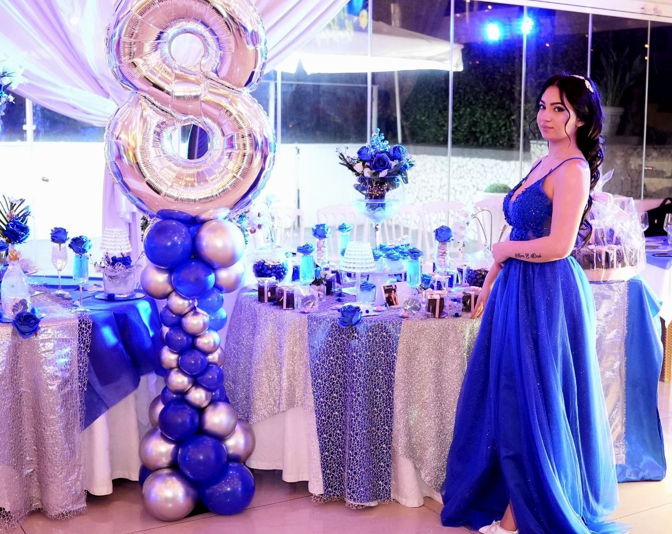 Una donna con un vestito blu è in piedi davanti a un tavolo decorato con palloncini blu e argento.
