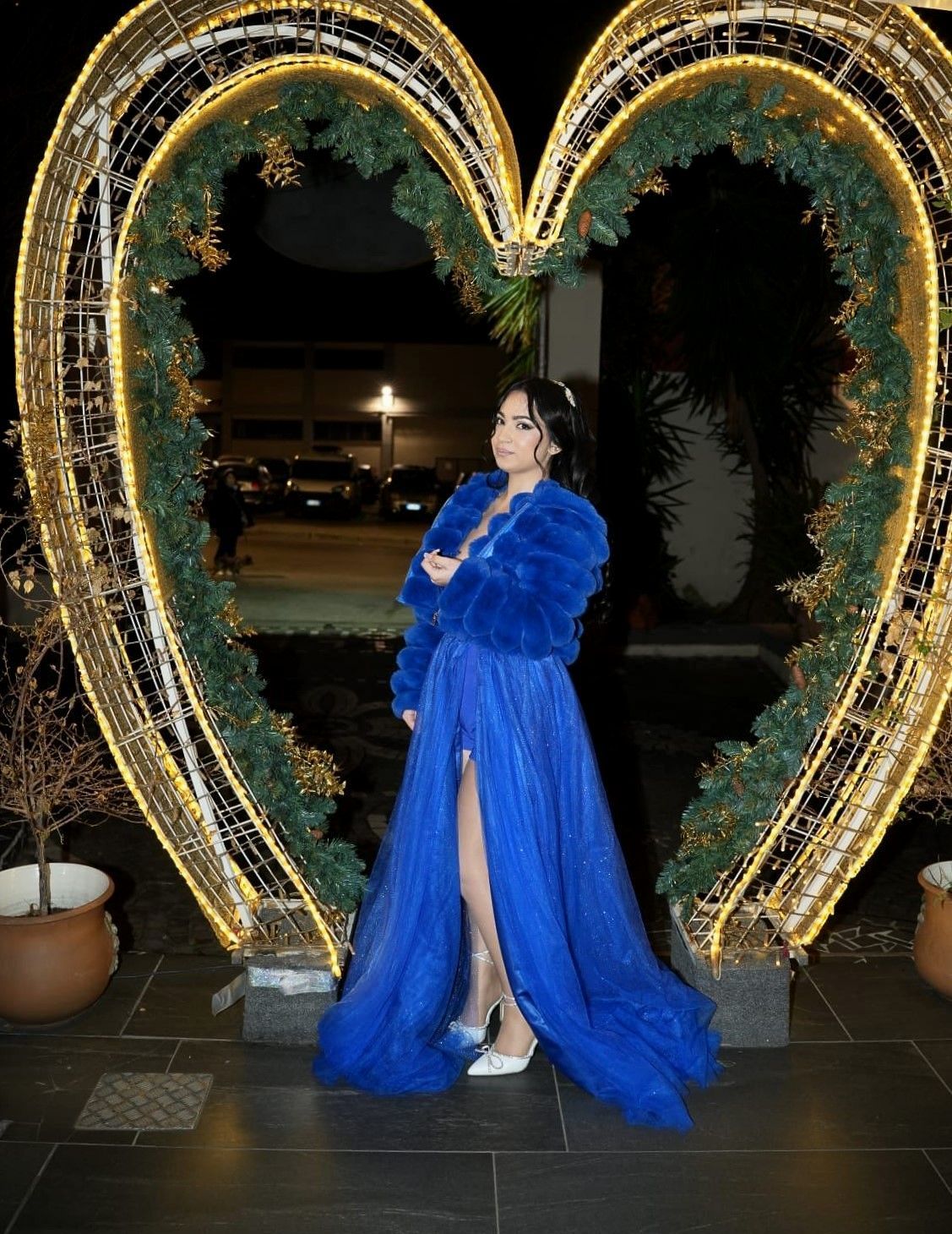 Una donna con un vestito blu è in piedi davanti a una decorazione a forma di cuore.